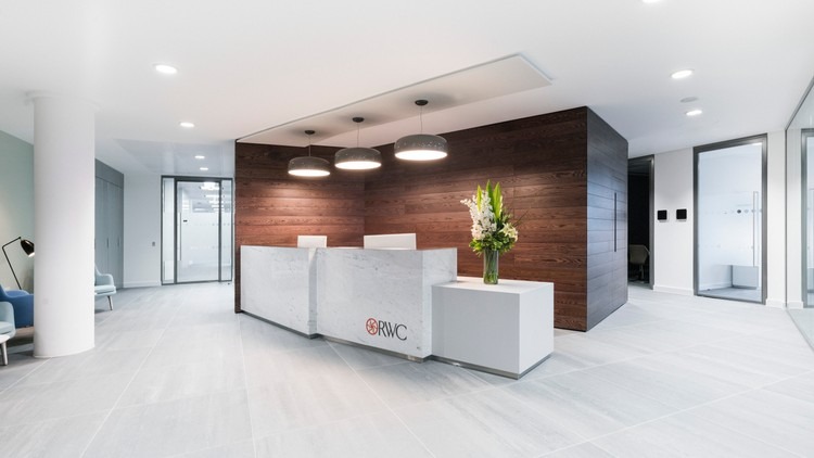Minimal lobby with walnut clad volume & stone desk — commercial interior design by Ab & Zen Interior